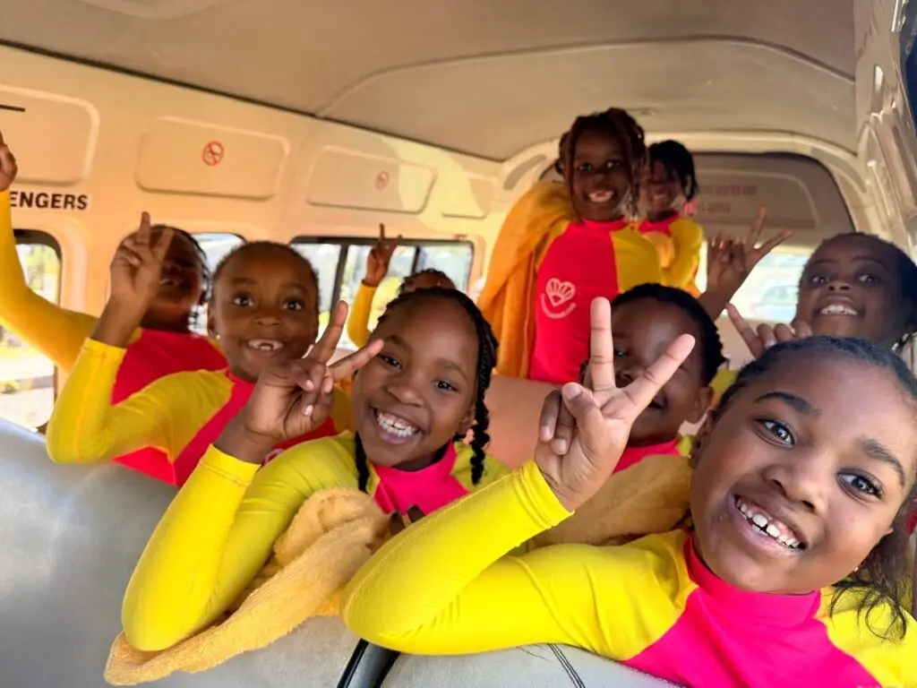 Kids in a bus smiling in Sunshine swimwear holding up peace sign